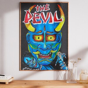 Puede incluir: Una obra de arte enmarcada que presenta una cara de diablo azul con cuernos amarillos y letras rojas que dicen "THE DEVIL". La obra de arte tiene un fondo negro y se exhibe en un mueble de madera.