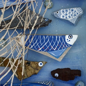 May include: A blue background with a white branch and five blue and white fish painted on wood. The fish are different sizes and shapes and have white and red details.