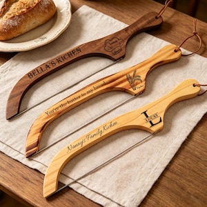 Può includere: Tre affettatrici per pane in legno con lame a filo e lacci in pelle per appenderle. L'affettatrice in legno scuro è incisa con BELLA'S KICHEN e un cappello da chef. Quella centrale mostra You're the butter to my bread e del grano. L'affettatrice in legno chiaro riporta Nanny's Family Kichen e LUCAS.