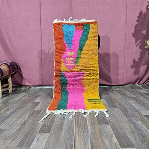 May include: A rectangular area rug featuring a high-pile texture with a vibrant, abstract geometric pattern. The design incorporates bold blocks of mustard yellow, bright pink, teal, and orange, finished with white fringe tassels at both ends.