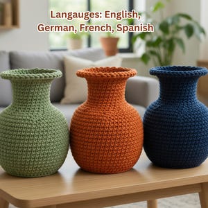 Puede incluir: Tres jarrones de ganchillo hechos a mano en verde, naranja y azul sobre una mesa de madera. Los jarrones tienen un cuerpo bulboso y un cuello acampanado. El texto "Langauges: English, German, French, Spanish" es visible.