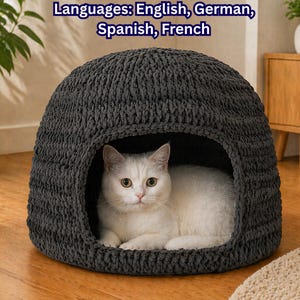 May include: A gray, dome-shaped cat bed made of thick, knitted material. A white cat with yellow eyes is inside the bed, looking directly at the camera. The image includes text at the top that says "Languages: English, German, Spanish, French."