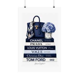 May include: A stack of six fashion books titled Chanel, Prada, Louis Vuitton, Vogue, Christian Dior, and Tom Ford. Atop the stack sits a dark blue handbag with a patterned scarf, a gold padlock, and a glass vase filled with blue hydrangea flowers.