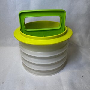 May include: A round, stackable Tupperware container system featuring a translucent white base with multiple tiered sections and a bright lime green lid that includes an integrated rectangular handle for easy carrying and storage.