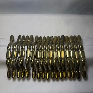 May include: A vintage gold-toned bracelet with a unique design. The bracelet features a series of curved, elongated links connected by rectangular segments. The metal has a slightly aged appearance, adding to its vintage charm.