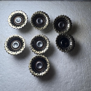 May include: Seven antique-style cabinet knobs with a sunflower design. The knobs are made of metal with a bronze finish, featuring a detailed petal pattern around a central, circular design. The knobs are arranged in a cluster.