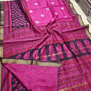 Puede incluir: Un textil rosa vibrante con patrones intrincados. La tela presenta una mezcla de diseños geométricos y de cachemira en tonos de rosa, negro y dorado. Los bordes están adornados con patrones detallados, creando una apariencia rica y texturizada.