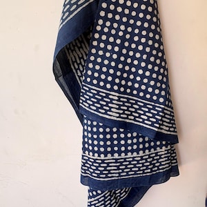 Peut inclure: Un textile bleu marine avec un motif à pois blancs et un motif de bordure. Le tissu est drapé, mettant en valeur le contraste entre le bleu foncé et les pois blancs. Il s'agit probablement d'une écharpe ou d'un accessoire similaire.