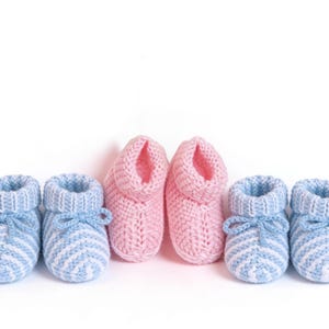 May include: Three pairs of knitted baby booties in soft pastel colors. Two pairs are light blue with white stripes and bow ties, and one pair is pink. The booties are arranged on a white background.