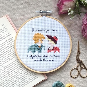 May include: A circular cross-stitch embroidery with the quote "If I loved you less, I might be able to talk about it more." The design shows two figures, stitched in various colours, in a romantic pose.