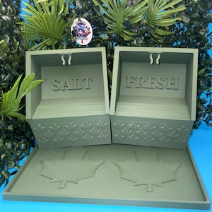 May include: Two sage green storage containers with open fronts, each featuring a small hook at the top. One container is labelled SALT and the other FRESH. The exterior surfaces are decorated with a repeating maple leaf pattern.