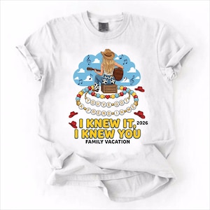 May include: A white t-shirt featuring a graphic of a person in a cowboy hat playing a guitar, sitting on a crate. Below are beaded necklaces with the text "YOU'VE GOT A FREND IN ME" and the printed text "I KNEW IT, I KNEW YOU 2026 FAMILY VACATION".