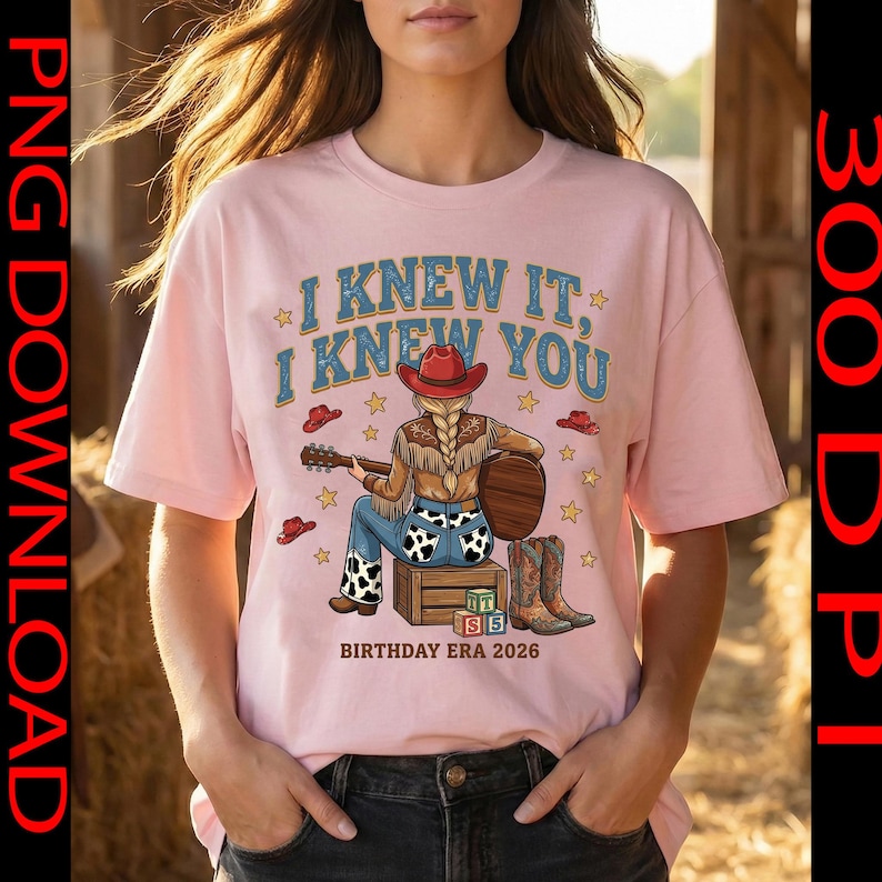 May include: A light pink t-shirt featuring a graphic of a person with a blonde braid wearing a red cowboy hat, fringe jacket, and cow-print jeans, sitting on a crate playing a guitar. Text reads I KNEW IT, I KNEW YOU and BIRTHDAY ERA 2026.
