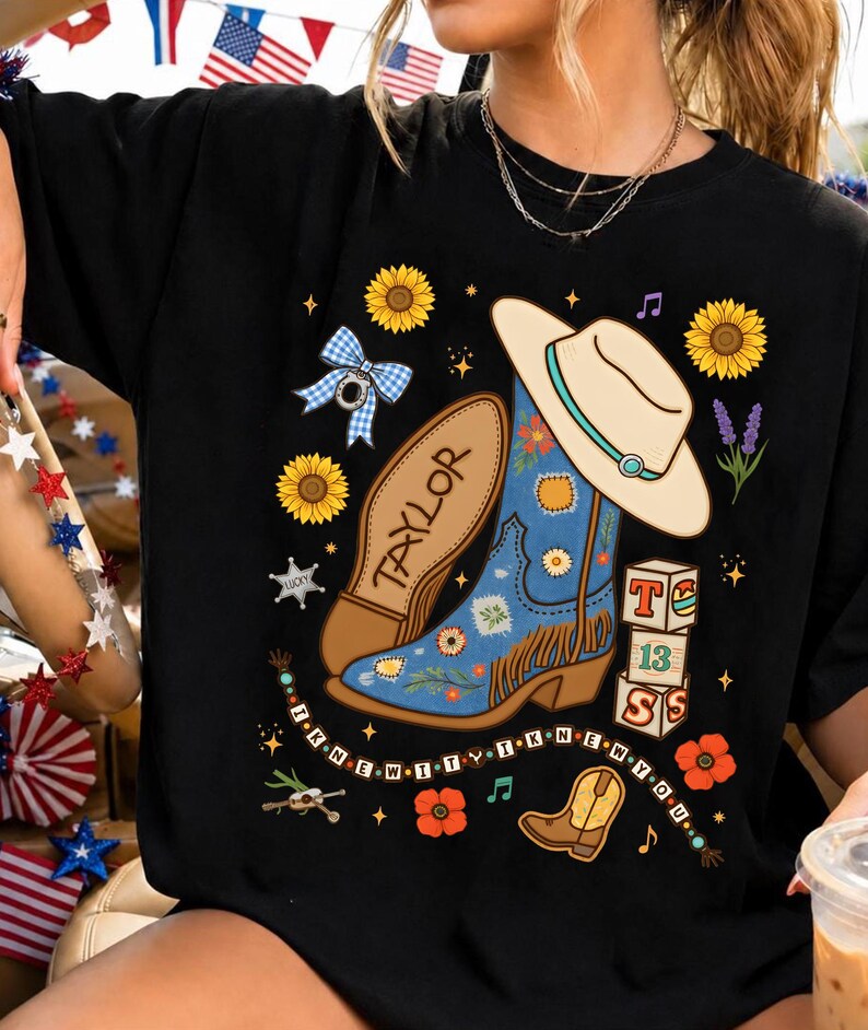 May include: A black t-shirt featuring a graphic print of a blue cowboy boot with fringe, a beige cowboy hat, sunflowers, a blue gingham bow, and blocks labeled T, 13, and S. The text "TAYLOR" and "I KNEW IT WHEN YOU" are printed on the shirt.