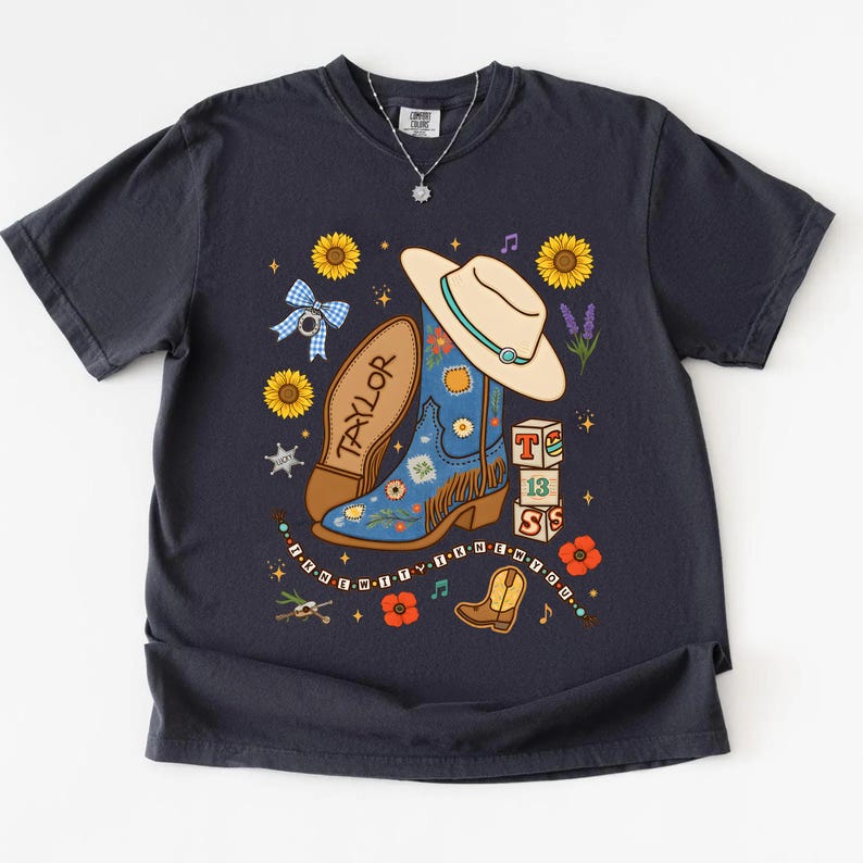 May include: A dark charcoal gray t-shirt featuring a graphic print of a blue cowboy boot, a beige hat, sunflowers, a blue gingham bow, and blocks with the text T, 13, S. The text "I KNEW IT I KNEW YOU" is printed in a curved line at the bottom.