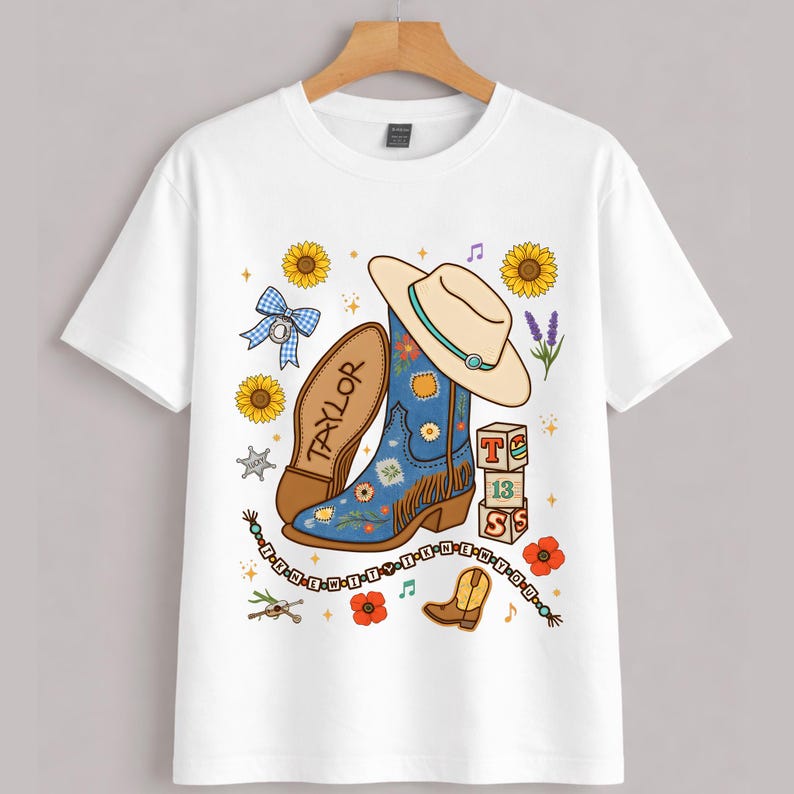 May include: A white short-sleeve t-shirt featuring a graphic print of a blue cowboy boot, a beige cowboy hat, sunflowers, a blue gingham bow, alphabet blocks spelling T-13-S, and a beaded string with the text I-R-N-E-W-I-T-T-Y-I-K-N-E-W-Y-O-U.