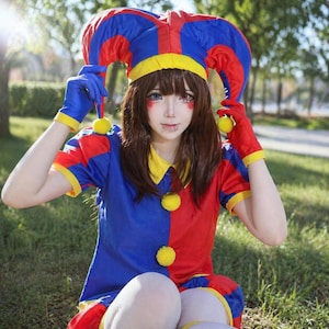 May include: A colorful jester costume with a red, blue, and yellow color scheme. The outfit includes a matching hat, gloves, and a collared shirt. The costume has yellow pom-poms and is worn outdoors.