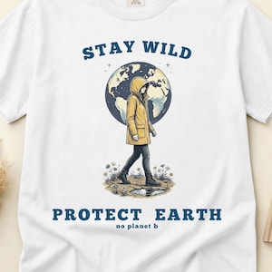 Op de afbeelding: Wit T-shirt met de blauwe tekst "Stay Wild Protect Earth". De afbeelding toont een persoon in een gele jas die voor een wereldbol loopt. De woorden "no planet b" staan eronder.
