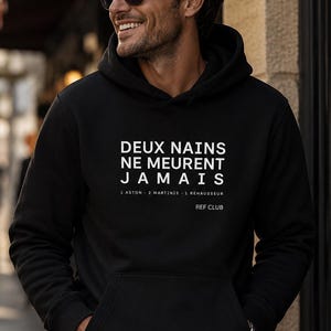 May include: A black hooded sweatshirt featuring white text that reads DEUX NAINS NE MEURENT JAMAIS, followed by 1 ASTON 2 MARTINIS 1 REHAUSSEUR and REF CLUB. The garment has long sleeves, a front kangaroo pocket, and a ribbed hem and cuffs.