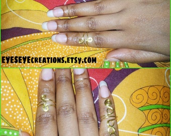 May include: A set of gold wire rings worn on the fingers of a hand. The rings are made of thin wire that is twisted and shaped into different designs. The rings are worn on the index, middle, and ring fingers.