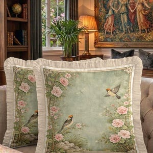 Può includere: Due cuscini quadrati decorativi con un design floreale e di uccelli vintage. I cuscini presentano uno sfondo verde chiaro con fiori rosa e uccelli. I bordi sono rifiniti con una balza color crema.