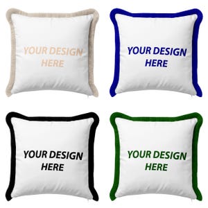 May include: Four square decorative pillows with white fabric and different colored trim. Each pillow has the text "YOUR DESIGN HERE" printed on the front. The trim colors are beige, blue, black, and green.