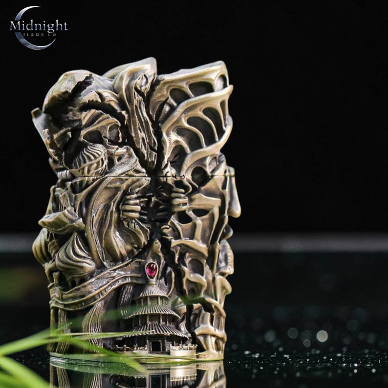 K&ouml;nnte beinhalten: Ein aufwendig geschnitztes Feuerzeug in Bronzefarbe mit detailliertem Reliefdesign. Das Feuerzeug zeigt eine Struktur im Pagodenstil, Figuren und einen roten Edelstein. Die Oberseite des Feuerzeugs hat ein Design, das einem Fl&uuml;gel &auml;hnelt. Das Logo "Midnight Trade Co" ist sichtbar.