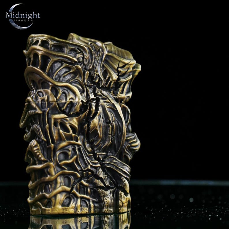 K&ouml;nnte beinhalten: Ein detailliertes, bronzefarbenes Feuerzeug mit einem komplizierten, strukturierten Design. Das Feuerzeug hat ein komplexes, skulpturales Aussehen mit dunklem Hintergrund. In der oberen linken Ecke steht der Text "Midnight Tide Co."