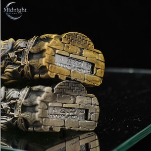 K&ouml;nnte beinhalten: Zwei Zippo-Feuerzeuge mit Backstein-Design. Eines ist bronzefarben, das andere silberfarben. Auf der Unterseite der Feuerzeuge ist der Text "A Zippo 20 BRADFORD, PA. MADE IN USA" eingraviert. Das Logo von Midnight Flame Co. ist sichtbar.