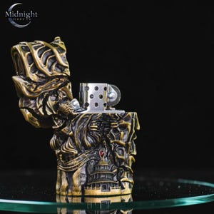 K&ouml;nnte beinhalten: Ein antiker Feuerzeug im Bronze-Look mit aufwendigen Details. Das Feuerzeug hat ein detailliertes Reliefdesign mit einer Pagode und anderen architektonischen Elementen. Die Oberseite ist ge&ouml;ffnet und zeigt den silberfarbenen Feuerzeugmechanismus. Der Markenname "Midnight" ist sichtbar.