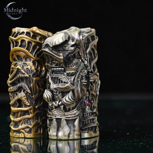 K&ouml;nnte beinhalten: Zwei aufwendig geschnitzte Metallboxen, eine goldene und eine silberne, mit detaillierten Reliefdesigns. Die Boxen weisen verzierte Muster und einen kleinen, roten Edelstein auf. Das Logo von Midnight Trade Co. ist oben links sichtbar.