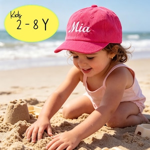 Puede incluir: Una gorra de béisbol de pana rosa brillante con el nombre Mia bordado en letra blanca en la parte delantera. Un gráfico ovalado amarillo en la esquina superior izquierda muestra el texto negro Kids 2-8 Y, indicando el rango de edad.
