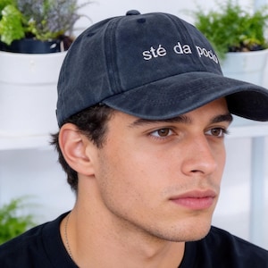 Puede incluir: Gorra de béisbol azul oscuro con el texto bordado "sté da poco" en blanco. La gorra tiene una visera curva y un botón en la parte superior. El sombrero está hecho de un material suave y desgastado.