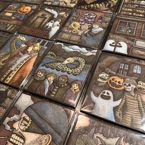 May include: A collection of illustrated cards featuring various spooky and Halloween-themed designs. The artwork includes ghosts, pumpkins, bats, and other eerie characters, all rendered in a detailed, cartoonish style with a variety of colors.
