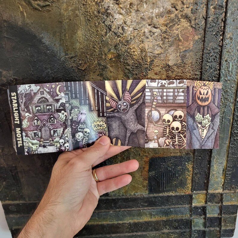 May include: A folded paper featuring a series of spooky illustrations. The images include a haunted house, skeletons, a bat-like creature, and a pumpkin-headed figure. The text "Starlight Motel" is visible on the left side of the paper.