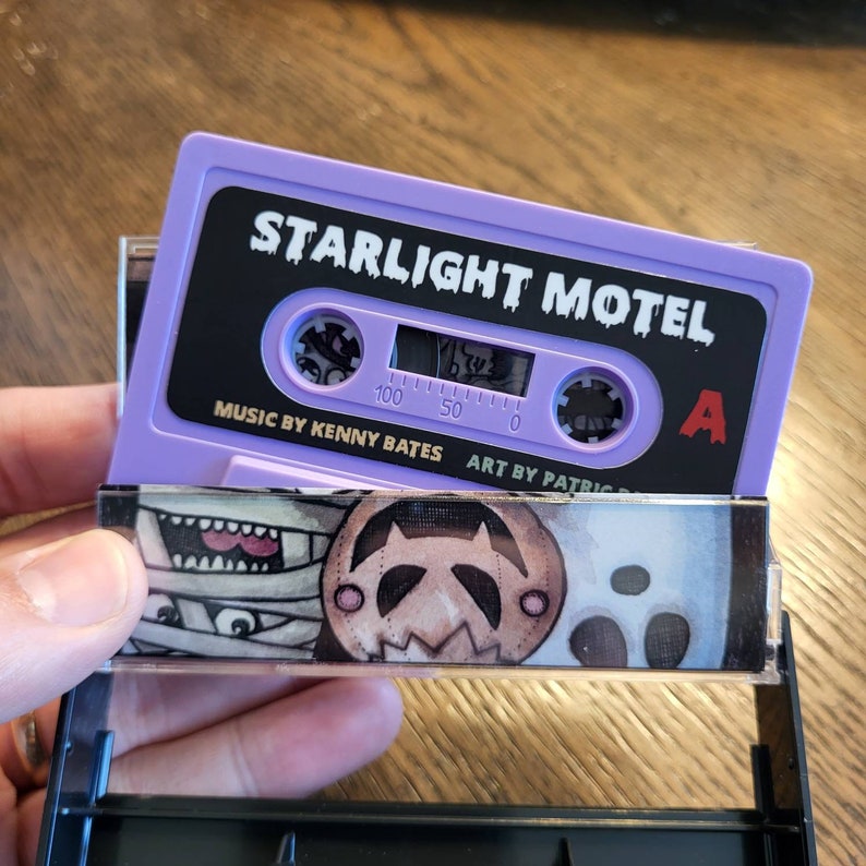 May include: A purple cassette tape labeled "STARLIGHT MOTEL" with black text. The cassette case has a colorful illustration of cartoon characters. The text "MUSIC BY KENNY BATES" and "ART BY PATRIC" are also visible.