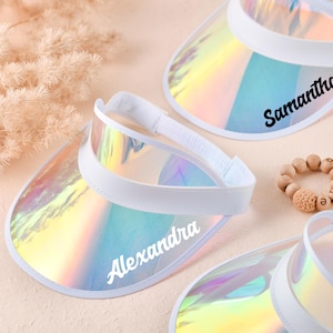 May include: Iridescent visor with a white headband and brim. The visor has the name "Alexandra" printed on it in black script. A wooden bead bracelet with the letter "e" is also visible.