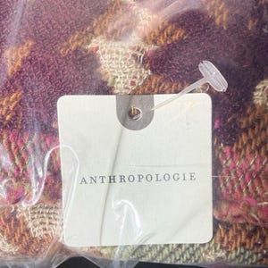 May include: A colorful scarf with a woven pattern in shades of purple, pink, orange, and green. The scarf is packaged in a clear plastic bag with a tag that reads "ANTHROPOLOGIE".