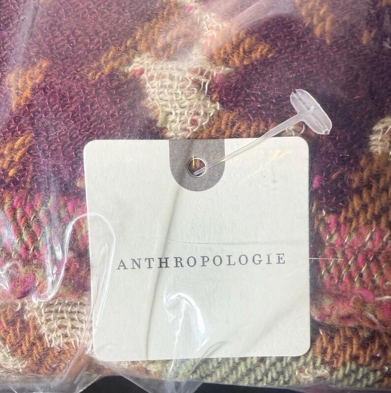 May include: A colorful scarf with a woven pattern in shades of purple, pink, orange, and green. The scarf is packaged in a clear plastic bag with a tag that reads "ANTHROPOLOGIE".