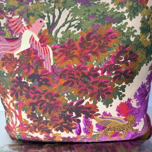 May include: A decorative pillow with a vibrant botanical design. The pillow features a colorful print of a bird, a leopard-like creature, and lush foliage in shades of pink, green, and purple. The pillow has a magenta border.