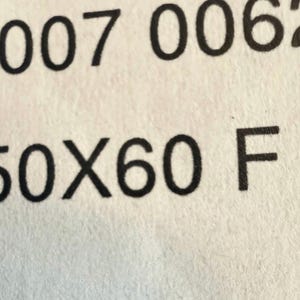 May include: Close-up of a white paper with black text. The text includes the numbers "00007 0062" on top, and "/ 50X60 F" below. The paper has a slightly textured surface.