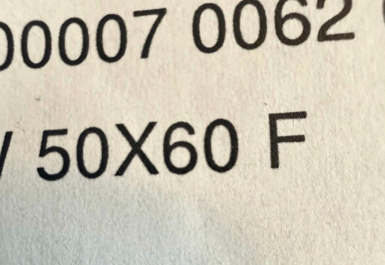 May include: Close-up of a white paper with black text. The text includes the numbers "00007 0062" on top, and "/ 50X60 F" below. The paper has a slightly textured surface.