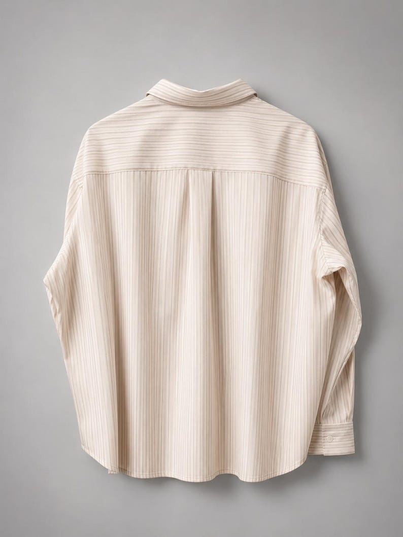 Puede incluir: Una camisa de manga larga con botones en color beige claro con finas rayas verticales marrones. La camisa presenta un cuello cl&aacute;sico, un canes&uacute; trasero con un pliegue central y pu&ntilde;os abotonados, mostrando la vista posterior.