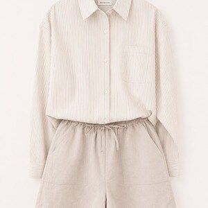 Puede incluir: Una camisa de manga larga abotonada con un patr&oacute;n de rayas verticales en beige y blanco, cuello y bolsillo en el pecho, combinada con pantalones cortos beige con cintura el&aacute;stica, cord&oacute;n ajustable y dos bolsillos delanteros. La etiqueta dice RIVAVIVA.