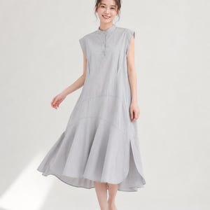 Può includere: Un abito midi senza maniche color grigio chiaro con colletto alla coreana, un'abbottonatura parziale sul davanti e una gonna svasata con orlo curvo. L'abito presenta una silhouette rilassata con una cucitura centrale e spacchi laterali.