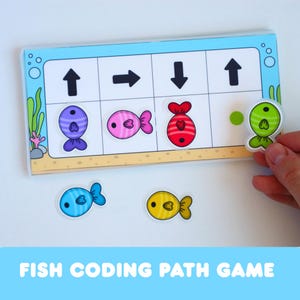 May include: A rectangular educational game board featuring a grid with black directional arrows and colourful fish illustrations. The board displays a purple, pink, and red fish in sequence, with a green fish being placed in the final empty slot.