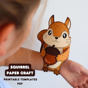 May include: A paper craft squirrel with brown fur and a dark brown acorn, featuring large black eyes and a cream-colored belly. The text SQUIRREL PAPER CRAFT PRINTABLE TEMPLATES PDF is displayed in a dark brown rounded rectangular box.