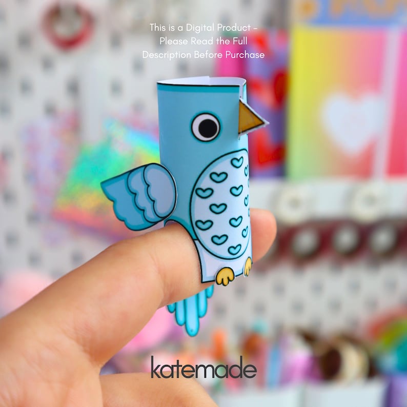 May include: A light blue paper bird finger puppet featuring a white belly with a heart pattern, a yellow beak, and black and white eyes. The text reads: This is a Digital Product - Please Read the Full Description Before Purchase and katemade.