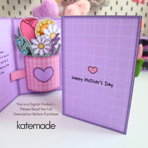 May include: A handmade Mother's Day card with a pop-up floral arrangement. The card features a pink gingham vase with a purple heart, holding paper flowers. The card is lavender with a grid pattern and the text "Happy Mother's Day".
