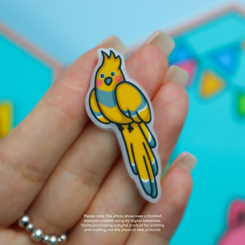 May include: A yellow and blue cartoon cockatiel sticker with a white outline. The bird has a crest, blue wing markings, and a long yellow tail. The sticker is held in a hand. Text at the bottom states the image is a digital example.